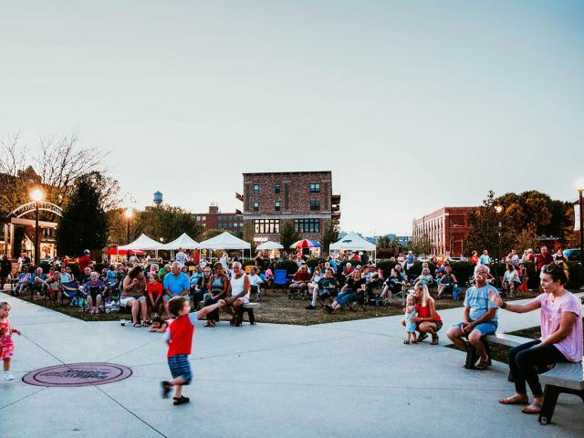 A Little boy try to skate on a road full of crowd.